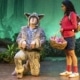 A girl watches as an actor dressed as a wolf kneels and howls