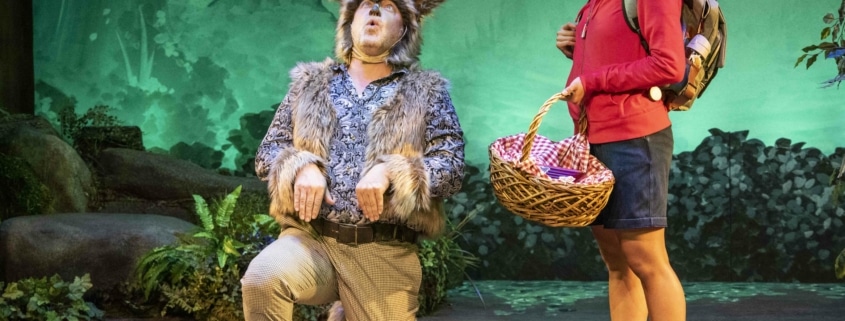A girl watches as an actor dressed as a wolf kneels and howls