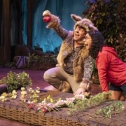 The wolf and Little Red kneel by a garden as the wolf holds up a vegetable