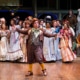 group of actors in period costumes performing on stage.