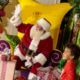 A child smiles with Santa surrounded by gifts