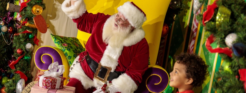 A child smiles with Santa surrounded by gifts