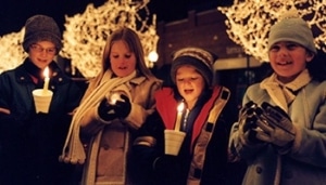 A group of people stand bundled together with lighted candles