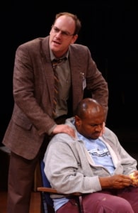 A man places his hands on a seated man's shoulders