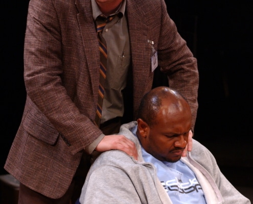 A man places his hands on a seated man's shoulders