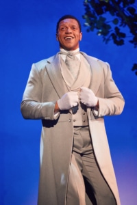 A man in a silver suit smiles onstage in My Fair Lady