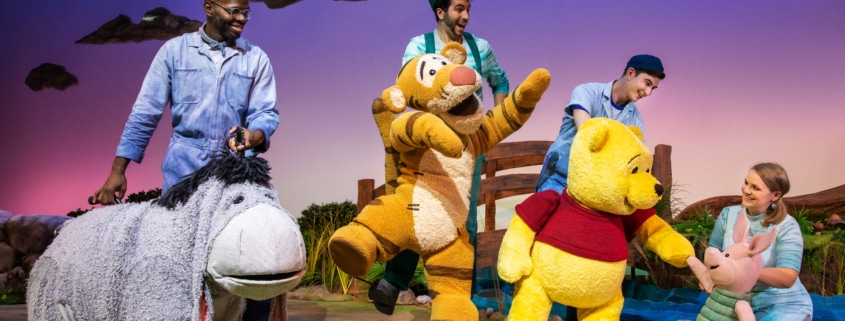 The cast and puppets of Winnie the Pooh pose onstage