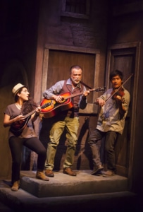 Three musicians stand together playing their instruments in Appogiatura