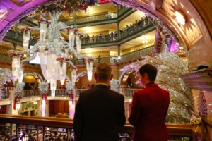 A couple watches the lobby of the Brown Palace Hotel from a balcony heavily decorated with holiday ornaments