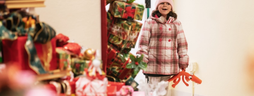 A little girl smiles as she looks into a room filled with gifts at Camp Christmas