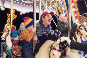 A man shouts with joy with his children as they ride the carousel at Camp Christmas