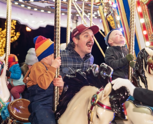 A man shouts with joy with his children as they ride the carousel at Camp Christmas