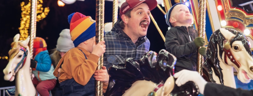 A man shouts with joy with his children as they ride the carousel at Camp Christmas