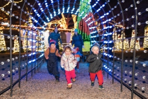 A group of children run through a lighted archway at Camp Christmas