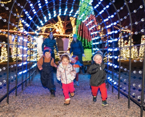 A group of children run through a lighted archway at Camp Christmas