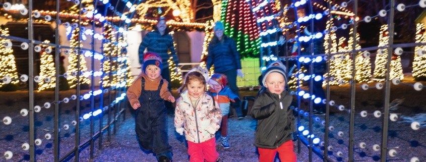 A group of children run through a lighted archway at Camp Christmas