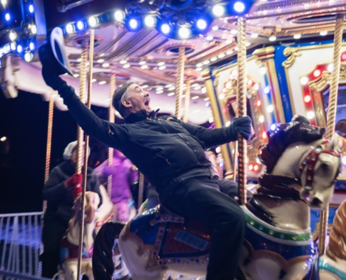 A man holds his hat in the air as he rides the carousel at Camp Christmas