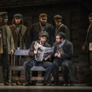 A group of men surround a newspaper in Fiddler on the Roof