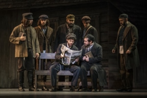 A group of men surround a newspaper in Fiddler on the Roof