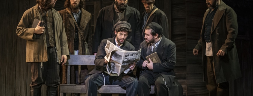 A group of men surround a newspaper in Fiddler on the Roof