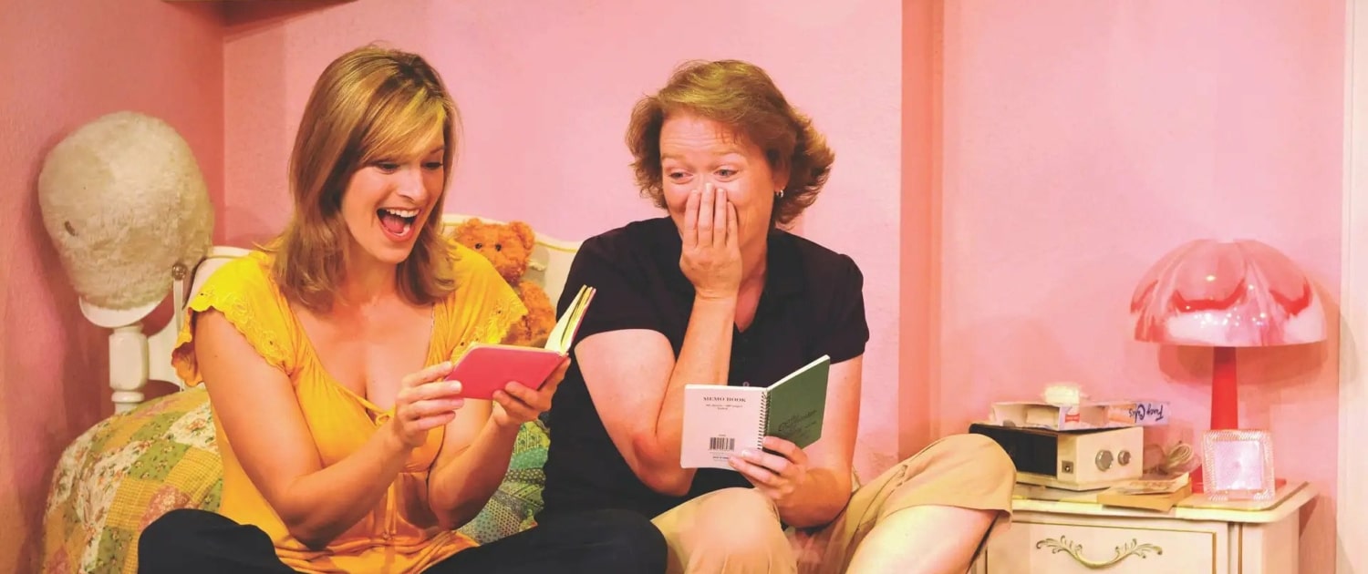 Linda Klein and Barbara Gehring sit on a bed reading their diaries in The Secret Comedy of Women