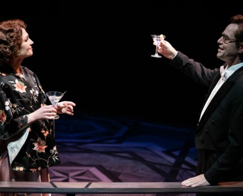 A woman in a floral shawl and a man in a tuxedo share a toast with martinis.