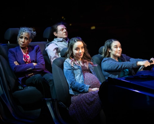 Three sisters ride in a car together. Celia drives while Tere sits annoyed in the backseat with the dead body.