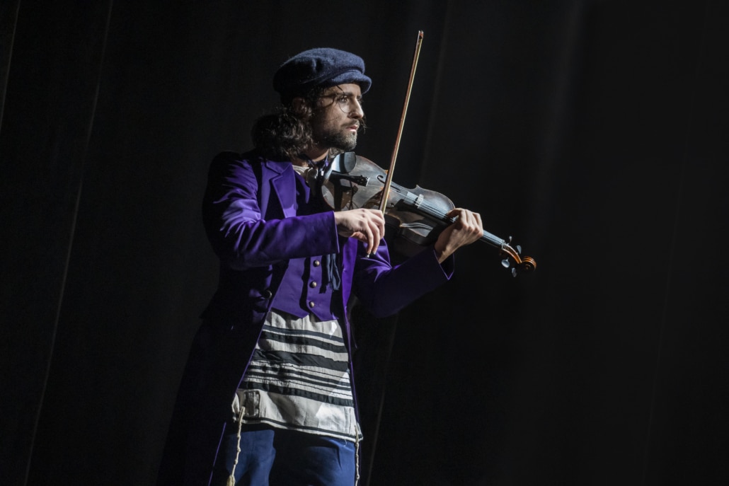 The Fiddler plays on a dark stage in Fiddler on the Roof