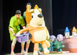 Mum is carrying a laundry basket, supported by actors in green jumpsuits.