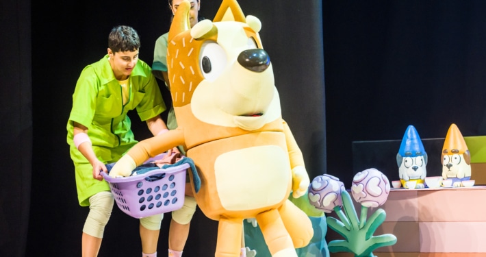 Mum is carrying a laundry basket, supported by actors in green jumpsuits.