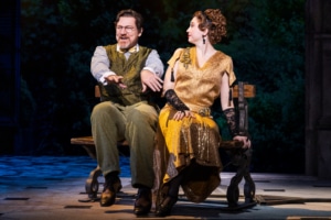 Vlad dances and smiles while seated on a bench with a young woman watching him