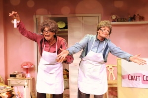 Linda Klein and Barbara Gehring dressed as older women show off their homemade crafts