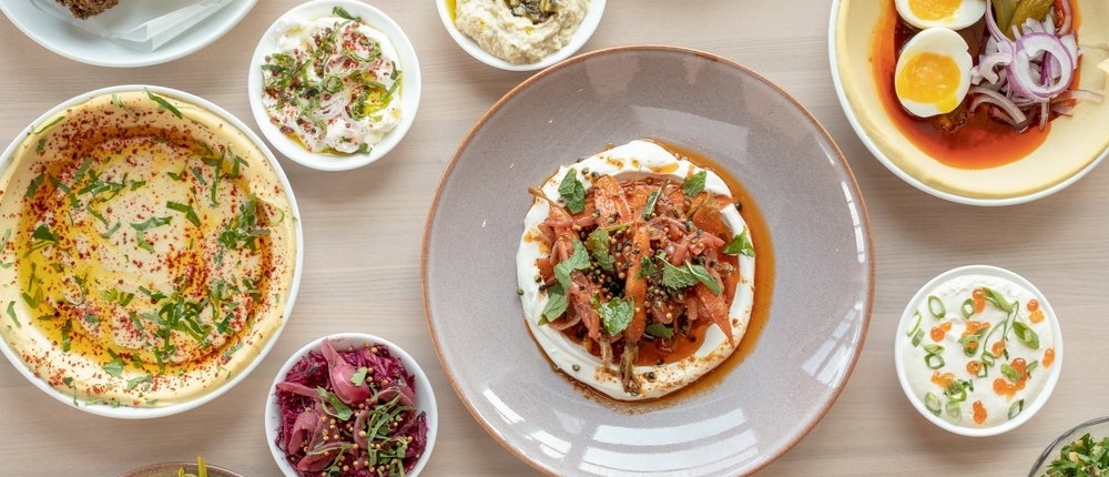 Several plates filled with Mediterranean food on a table at Safta