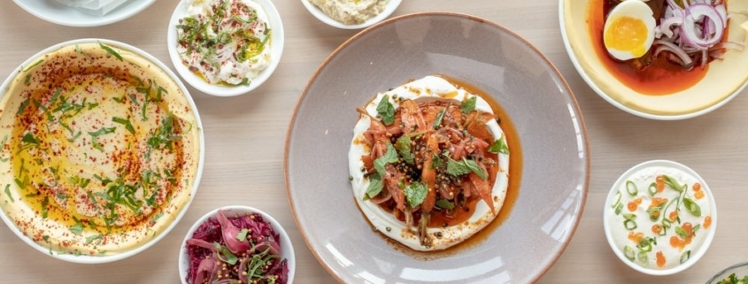 Several plates filled with Mediterranean food on a table at Safta