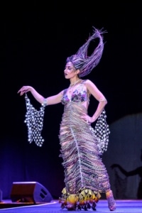 A model poses on the catwalk wearing a slinky gown, her hair intertwined with colorful wires in a towering updo