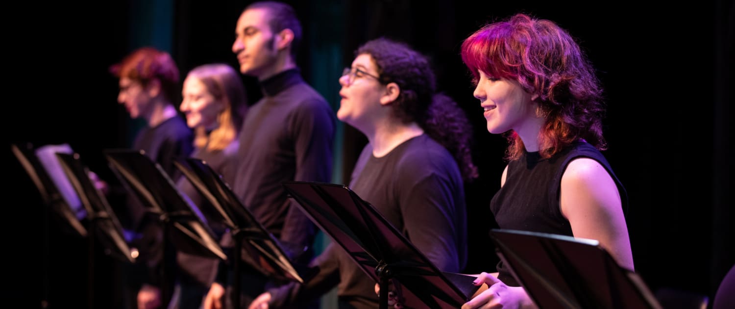 A row of actors standing at music stands wearing all black