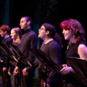 A row of actors standing at music stands wearing all black