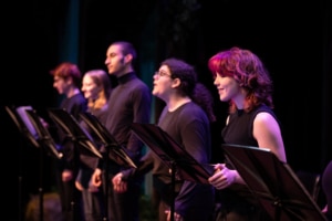 A row of actors standing at music stands wearing all black