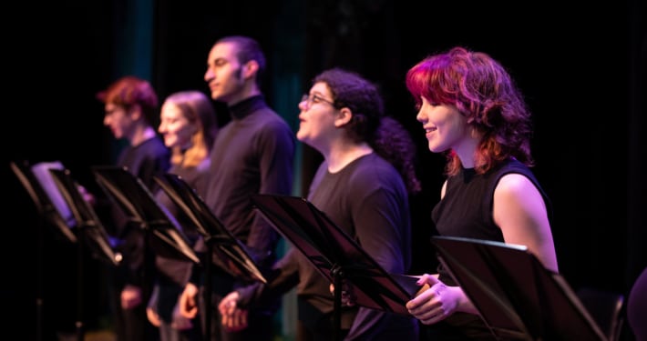 A row of actors standing at music stands wearing all black