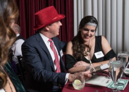 A couple wearing 1920's style costumes is seated at a dinner table, looking over clues