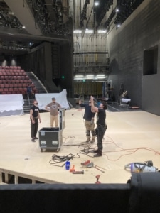 Lighting technicians stand onstage with wires for the load in for The Color Purple