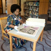 Jameka Lewis seated at a table flips through a large archive book at the Blair Caldwell African American Research Library