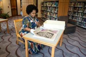 Jameka Lewis seated at a table flips through a large archive book at the Blair Caldwell African American Research Library