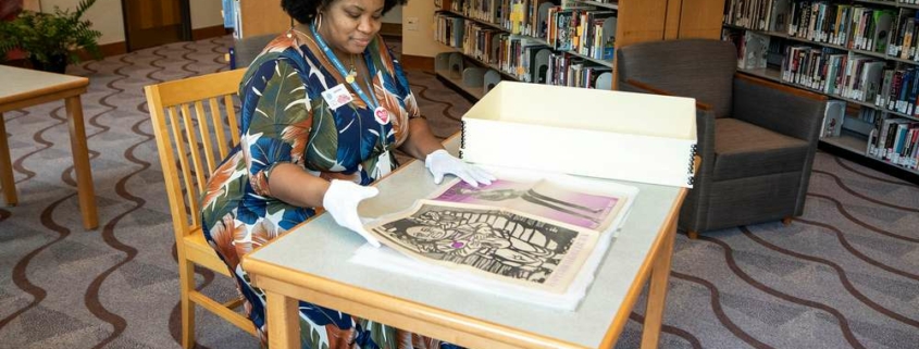 Jameka Lewis seated at a table flips through a large archive book at the Blair Caldwell African American Research Library