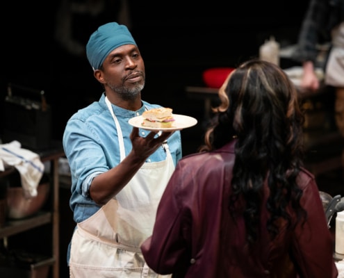 man holds offers a sandwich to a woman with a serene expression on his face.