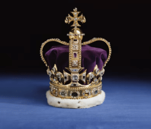 The Crown Jewels set on a blue table. The purple velvet crown is surrounded by gold and jeweled embellishment