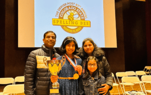 Spelling Bee Champion Aditi Muthukumar smiles with her family holding her trophy and medal