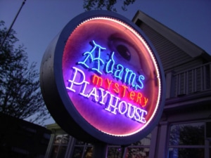 A lit up neon sign reading Adams Mystery Playhouse