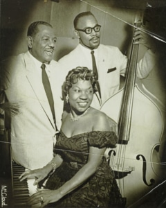 Charlotte Cowens sits at a piano with two other musicians