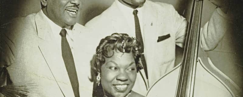 Charlotte Cowens sits at a piano with two other musicians